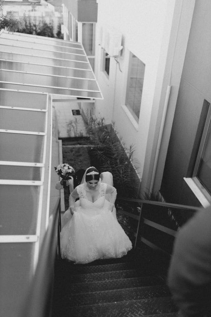 A bride elegantly descends a staircase, captured in black and white for timeless elegance.